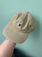 Load image into Gallery viewer, Beige cap with a small embroidered old english sheep dog held by a person against a light green background