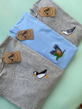 Load image into Gallery viewer, Three t-shirts with embroidered bird designs on a light green surface. puffin, kea and sea gull embroidery